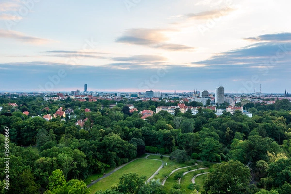 Fototapeta Aerial panorama of lush green park and distant cityscape under cloudy sunset sky