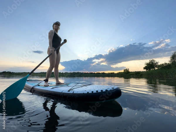 Fototapeta Paddleboarding at Sunset on a Tranquil Lake