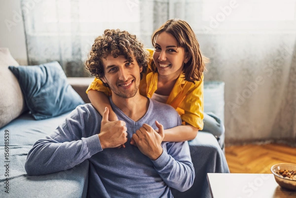 Fototapeta Portrait of young happy couple at home. They are looking at camera and smiling.