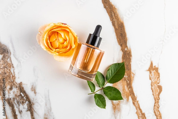 Obraz A transparent bottle with a dropper of serum, oil lies on an abstract marble background with the head of a tea rose. Natural moisturizing. top view