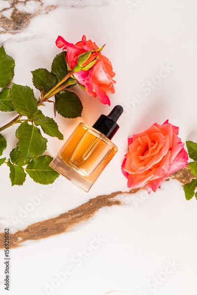 Obraz A natural beauty product in a clear dropper bottle on a marble abstract background among pink roses. vertical top view. A blank bottle mockup.