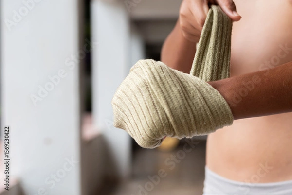 Fototapeta Close-up of a young Muay Thai fighter wrapping his hand with traditional cloth. The image captures detail and texture, highlighting strength, focus, and cultural authenticity.
