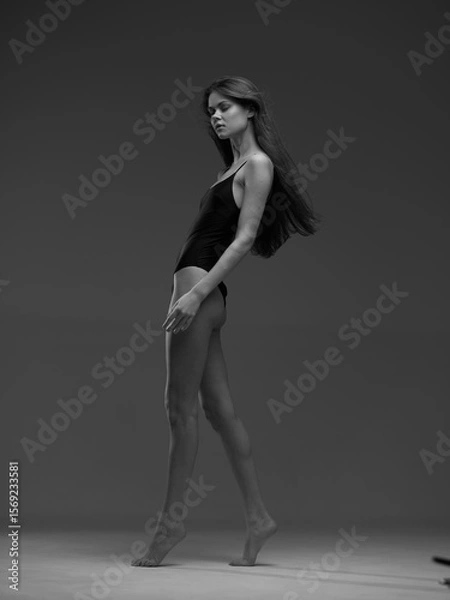 Fototapeta black and white woman walking gracefully in a simple black bodysuit with long hair, elegant pose, studio background, minimalist style, artistic mood