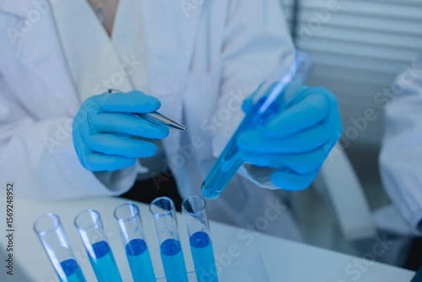 Fototapeta a female chemist is testing various liquid compounds in a lab, a scientist is doing research on the development, she wears a lab coat when she works in laboratory, test tube, scientific equipment