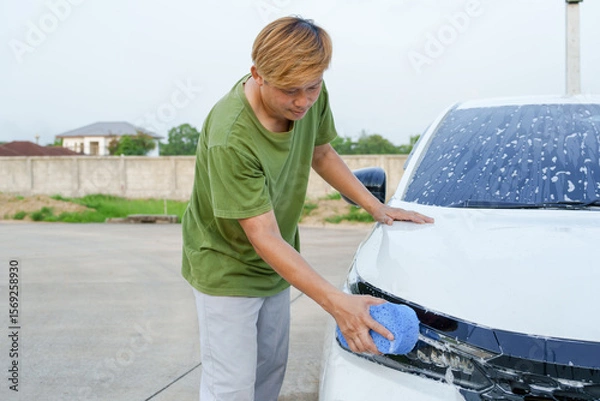 Fototapeta A smiling man is washing his car with soapy water under bright sunlight, showing his enthusiasm and joy in his daily work.