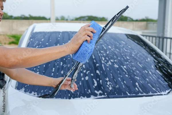 Fototapeta A smiling man is washing his car with soapy water under bright sunlight, showing his enthusiasm and joy in his daily work.