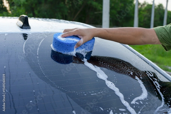 Fototapeta A smiling man is washing his car with soapy water under bright sunlight, showing his enthusiasm and joy in his daily work.