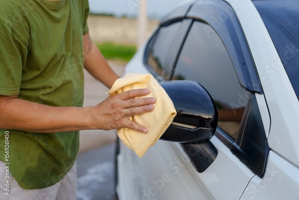 Fototapeta A smiling man is washing his car with soapy water under bright sunlight, showing his enthusiasm and joy in his daily work.