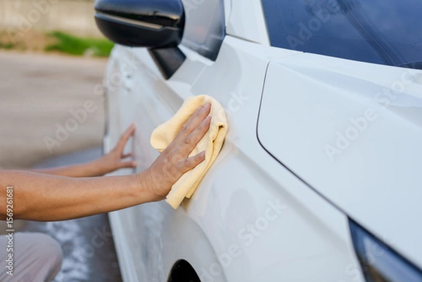 Fototapeta A smiling man is washing his car with soapy water under bright sunlight, showing his enthusiasm and joy in his daily work.