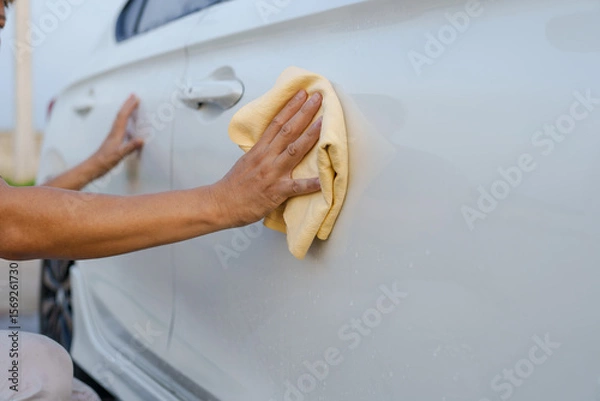 Fototapeta A smiling man is washing his car with soapy water under bright sunlight, showing his enthusiasm and joy in his daily work.