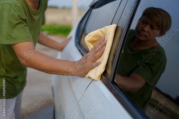 Fototapeta A smiling man is washing his car with soapy water under bright sunlight, showing his enthusiasm and joy in his daily work.