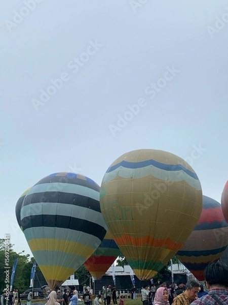 Fototapeta Colorful hot air balloons festival display distinct horizontal stripes are being inflated on the cloudy sky provide  backdrop. 