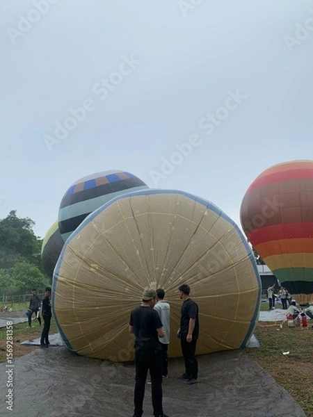 Fototapeta Colorful hot air balloons festival display distinct horizontal stripes are being inflated on the cloudy sky provide  backdrop. 