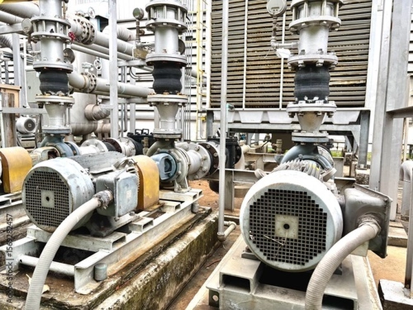 Obraz Industrial electric motor pumps installed outdoors with connected pipelines and valves, used in cooling systems, HVAC, and fluid transfer operations in factories or energy plants.