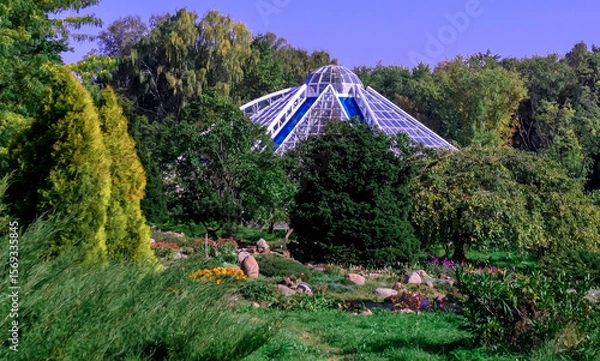 Fototapeta Beautiful botanical garden featuring a modern glass structure surrounded by lush greenery and colorful flowers