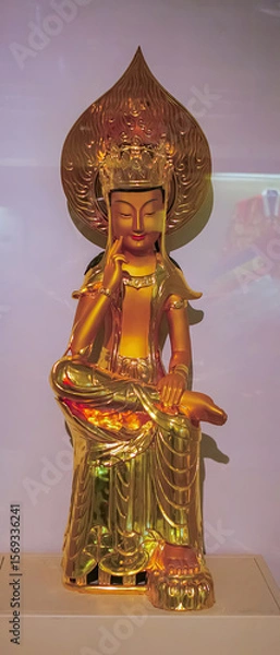 Fototapeta Beautiful golden statue of a Buddhist figure displayed in a museum gallery surrounded by soft lighting