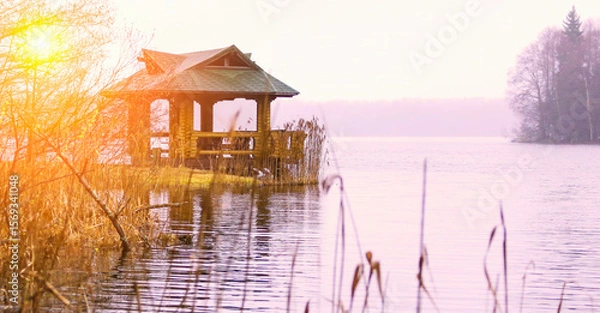 Fototapeta Serene lakeside gazebo at sunset surrounded by nature and reflections on the water