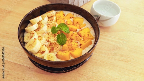 Fototapeta Smoothie bowl with slices of bananas, mango, and mint on a light wooden table showing clean eating and healthy living to promote wellness