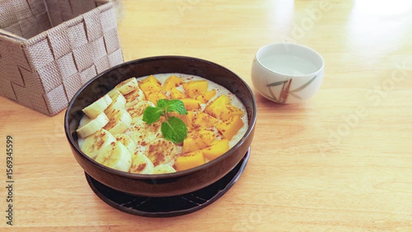 Fototapeta A smoothie bowl with banana and mango topped with mint leaves, set on a light wooden table, healthy vegan breakfast