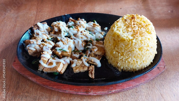 Fototapeta Sizzling plate of tofu sisig which is a vegetarian version of the traditional local Filipino dish from the Philippines, accompanied by a mound of java rice, served on a wooden table