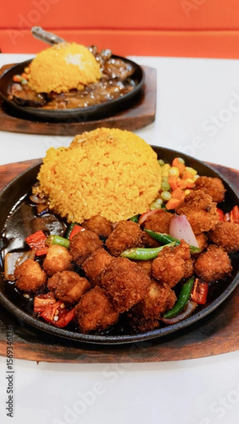 Fototapeta Fried tofu cubes and java rice served on a sizzling hot plate with mixed vegetables in a casual vegan dining setting