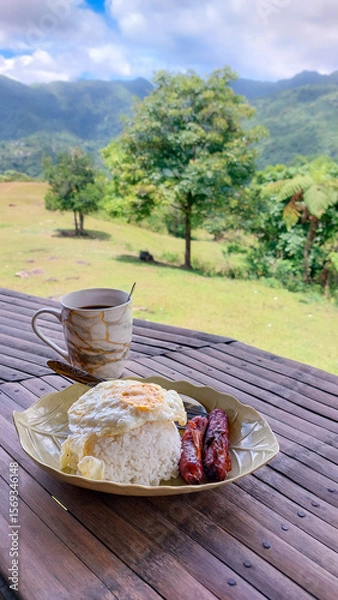 Fototapeta Filipino breakfast meal with rice, sausage, and fried egg served with coffee on a table overlooking a lush mountain landscape showing the calm of rural living