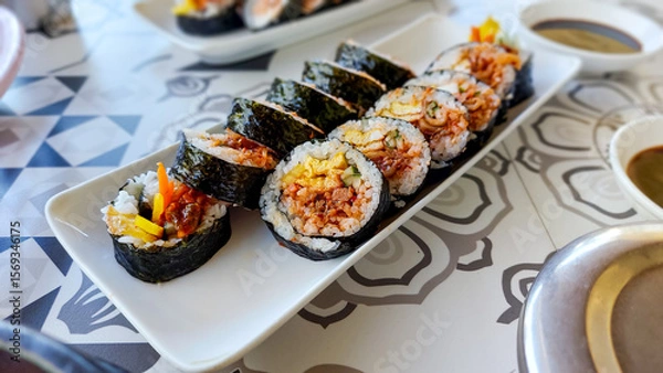 Fototapeta A plate of seaweed rice rolls or gimbap with vibrant fillings served on a patterned table, traditional local South Korean dish