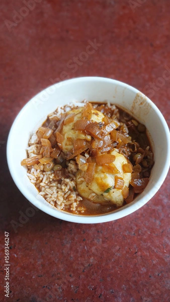 Fototapeta A bowl of potato dumplings with rice topped with caramelized onions on a red surface, a simple homecooked dish
