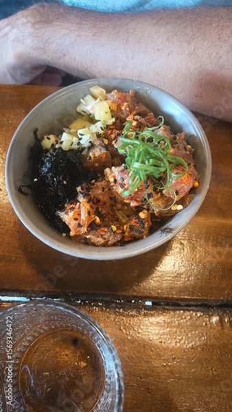 Fototapeta A poke bowl with tuna, seaweed, chives, and sesame seeds on a wooden table, an authentic traditional local Hawaiian dish