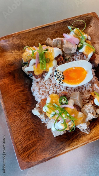 Fototapeta A wooden plate filled with brown rice, topped with tofu cubes, halved boiled egg and various colorful garnishes, creating a fresh and vibrant look for a healthy vegetarian meal