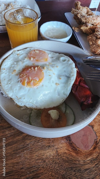 Fototapeta A Filipino breakfast bowl with fried eggs, hot dog, and rice served with crispy chicken and a glass of orange juice