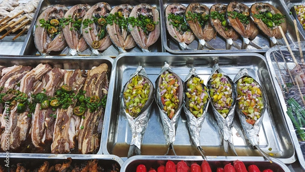 Fototapeta Marinated bangus or milkfish and marinated pork with vegetables displayed in trays ready for grilling in a street food stall showing a glimpse of the Philippines local cuisine and culture