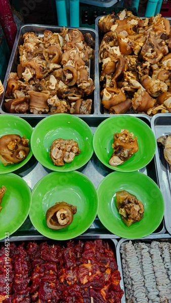 Fototapeta A display of pata or boiled pork knuckles, barbecue and isaw or chicken intestine skewers at a market stall. Authentic Filipino street food of the Philippines