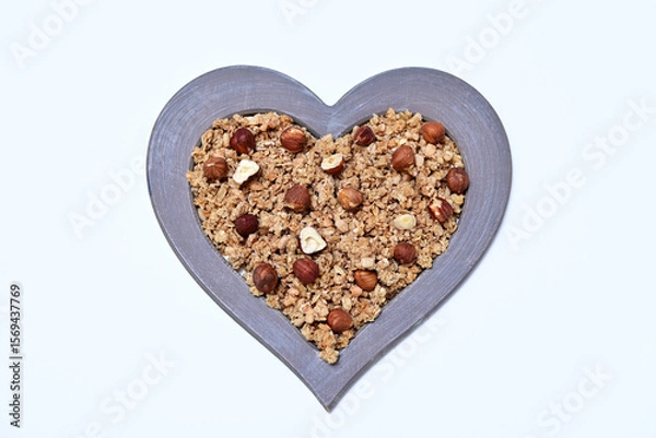 Fototapeta granola with whole hazelnuts in a heart shaped frame on a white background