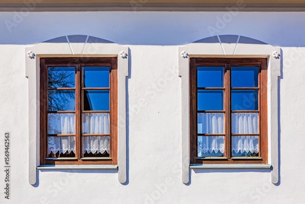 Fototapeta Charming wooden windows with lace curtains on white wall