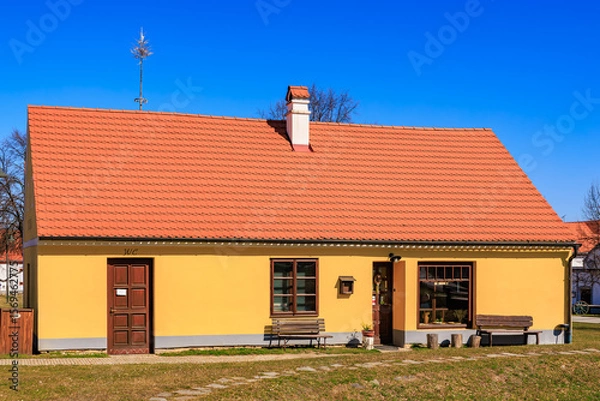 Fototapeta Charming small yellow house with red roof in sunny countryside setting under clear blue sky