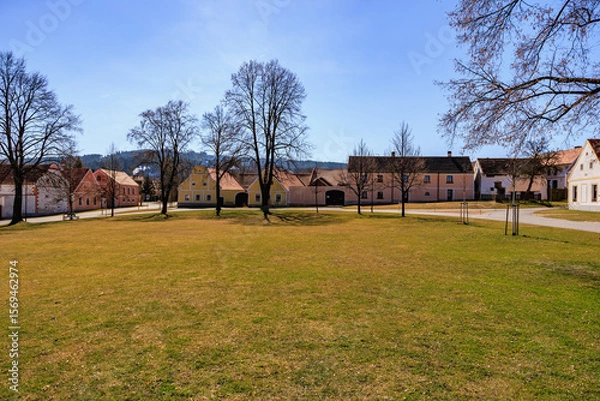 Fototapeta Charming european village square with historic houses and trees on a sunny day