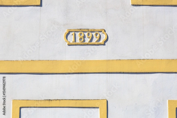 Fototapeta Architectural detail with 1899 date on yellow and white building facade