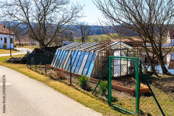 Fototapeta Rural greenhouse in countryside with bare trees and fenced pathway