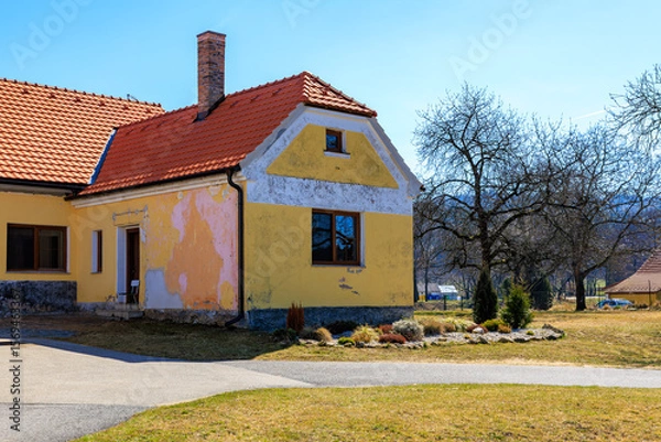 Fototapeta Charming rural cottage with red roof and weathered yellow walls in countryside landscape