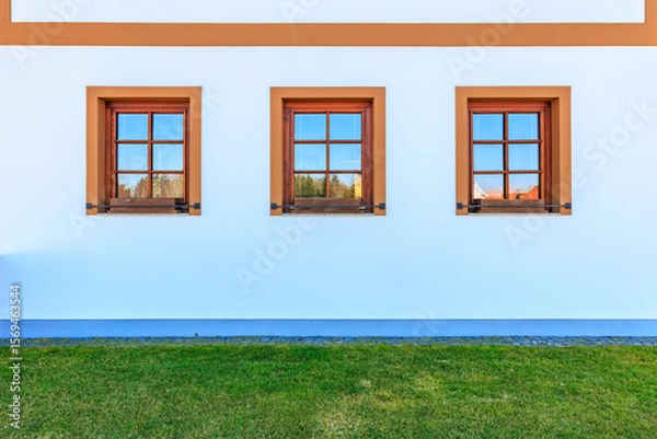 Fototapeta Symmetrical triple windows on white building with green grass lawn