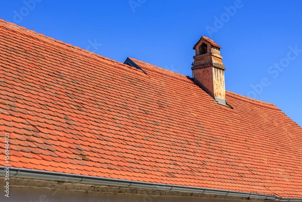 Fototapeta Red tiled roof with chimney under clear blue sky