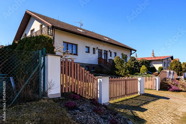 Fototapeta Suburban house with wooden fence and garden under clear blue sky