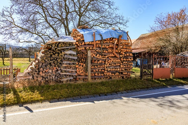 Fototapeta Rustic woodpile with tarp in countryside next to road on sunny day