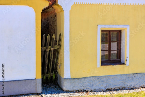Fototapeta Yellow wall with window and rustic fence in sunlit scene