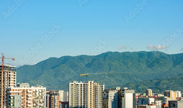 Fototapeta Urban skyline with mountain backdrop. Modern city high-rises set against a stunning backdrop of green mountains. The harmonious blend of urban and natural landscapes.