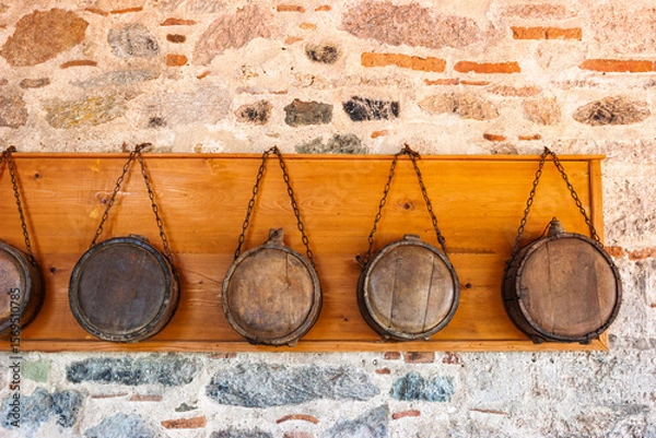 Fototapeta Row of traditional wooden canteens hanging on chains against stone monastery wall