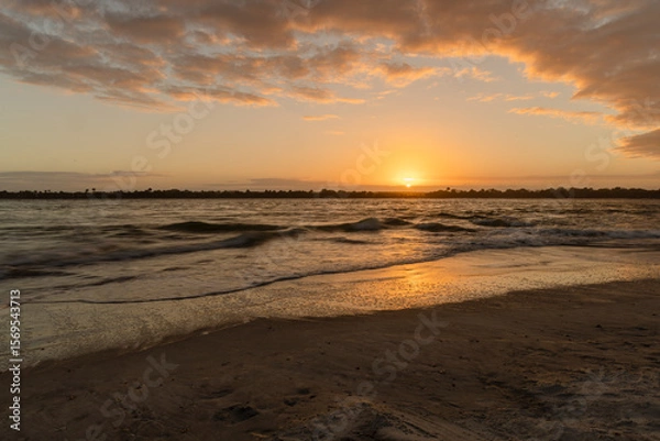 Fototapeta The sun setting over the Matanzas Inlet with clouds framing the picture and the sun reflecting in the water
