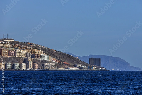 Obraz Mountains and buildings on the horizon on the shore of the blue Atlantic Ocean on the island of Tenerife under a clear sky	
