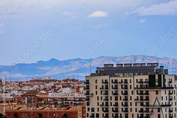 Obraz Diverse and colorful houses of a Spanish town with mountains on the horizon under a cloudy blue sky on a summer day	
